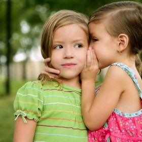 Two twin little sister girls whisper in ear